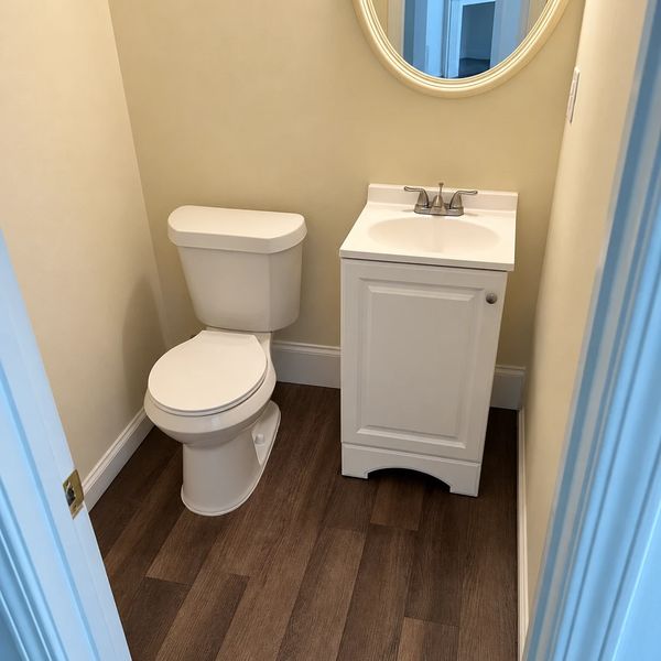 Half bath with plank flooring, a new toilet and a white vanity