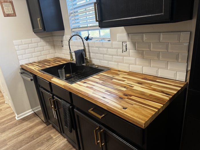 Kitchen with butcher block counters, black cabinets and a white subway tile backsplash