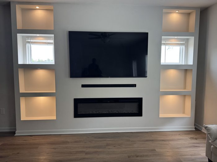 Media wall with lit shelf niches on both sides, a wall-mounted TV and an electric fireplace